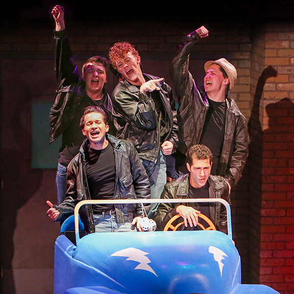 Photo from our 2015 production of Grease showing the boys in a small blue hotrod singing Greased Lightning.