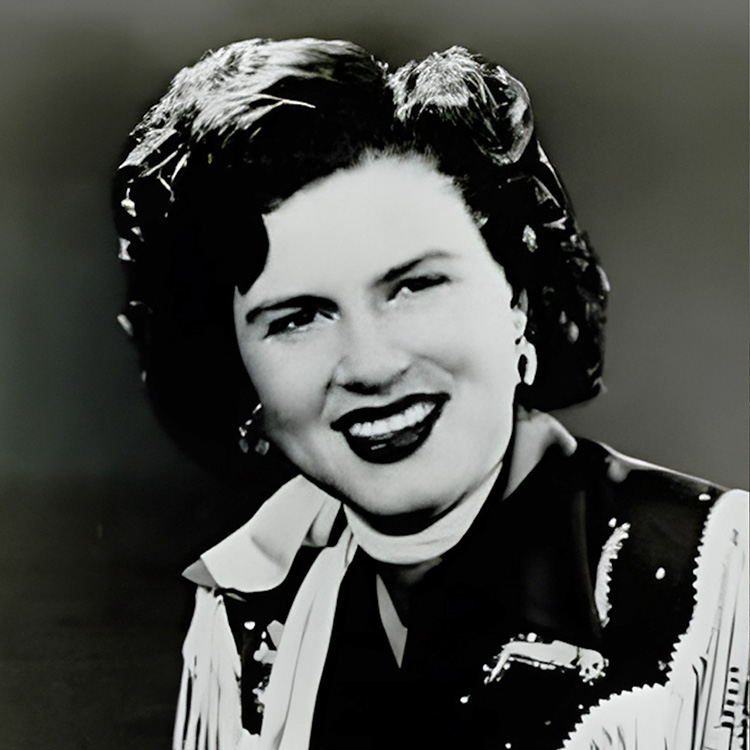 Promotional photo of Patsy Cline, posing in her iconic cowgirl outfit with white fringe.