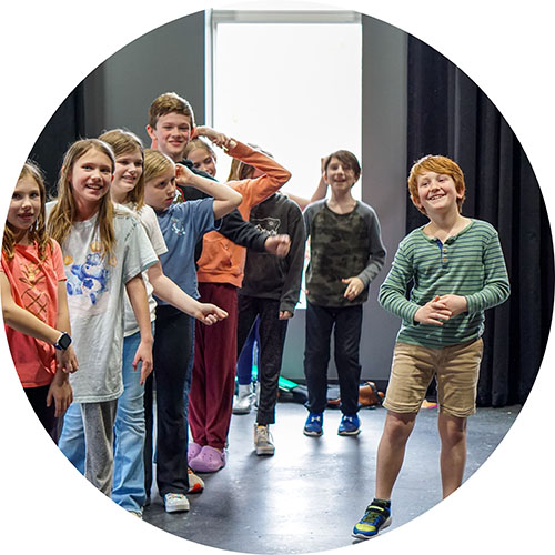 Photo from one of our kids workshops showing a line of kids all smiling and laughing, with another boy on the right, standing for his solo, smiling wide.