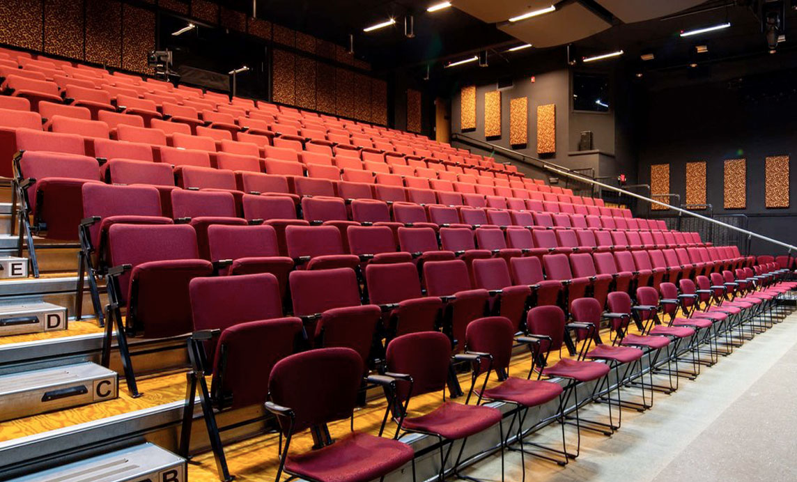 Photo of the seating at the New Stage Theater. Shows rows of red, cushioned seats and the stairs leading up to each row.