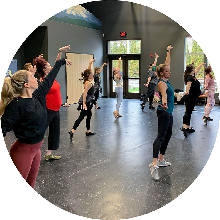 Photo from one of our Adult Dance classes showing the students mid dance number, posing with their left arms raised above their heads and their right arms out to the side.