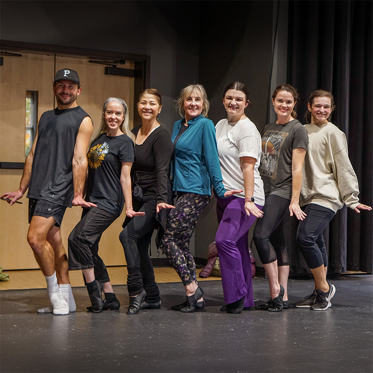 Photo of the students and teacher in our most recent dance class. THey are all posing together in a contraposto, one leg straight and the other bent position. Their hands are out to their sides, flat, like a jazz dance move.