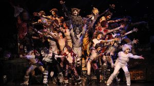 Photo of the 2011 production of Cats. The entire cast of over 20 performers is in a group formation, reaching their arms out toward the audience.