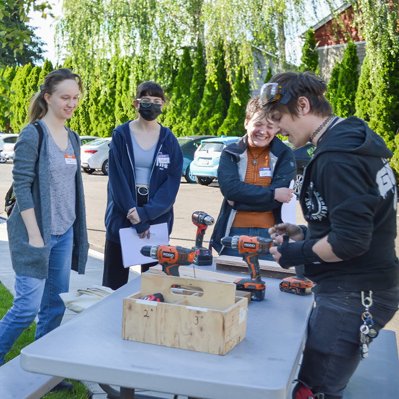 Photo of some of our latest interns, gathered around a table where our technical director, Raef Wheaton, demonstrating some of the differences between types of power drills.