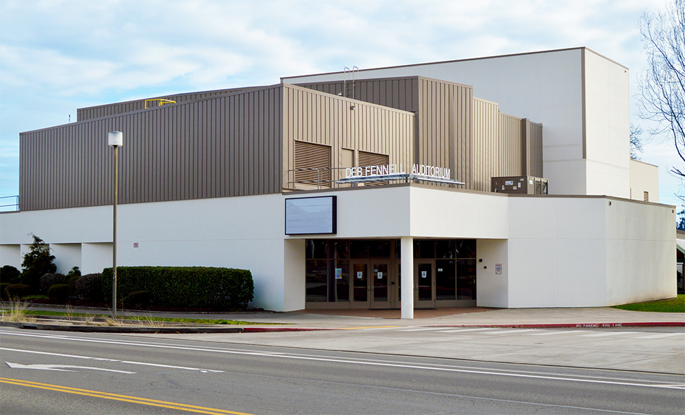 Photo of the front exterior of the Deb Fennell Auditorium. It is a tiered building with white walls, but the upper tiers have brown walls.