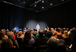 Photo from one of our past Cabarets, showing a performer up on a small stage in front of an intimate crowd.