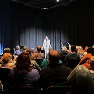 Photo from one of our past Cabarets, showing a performer up on a small stage in front of an intimate crowd.